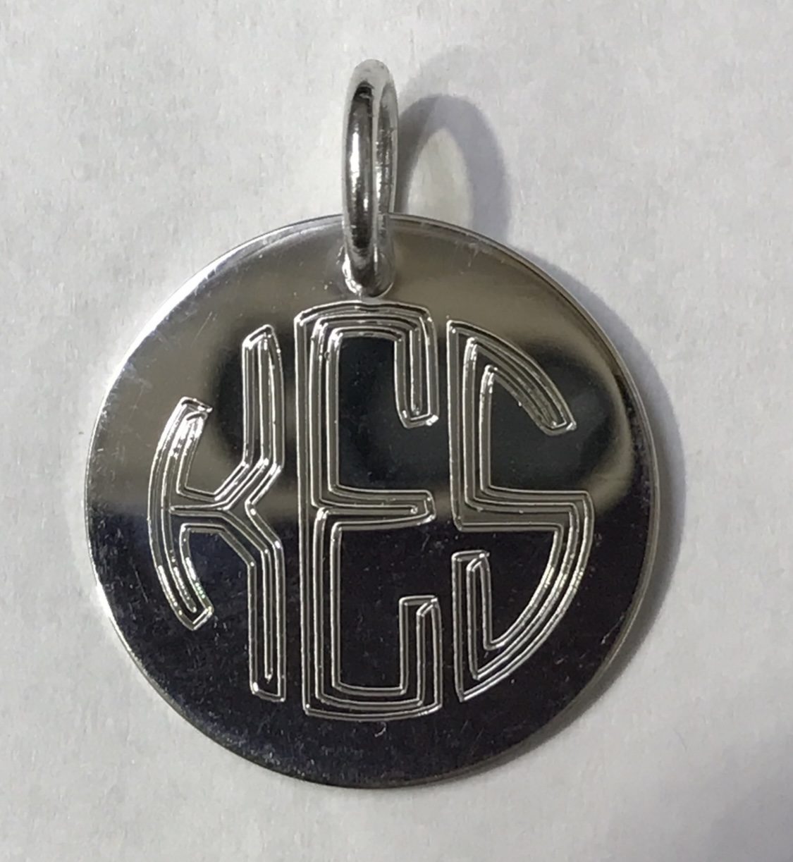 Round silver pendant engraved with an interlocking block monogram