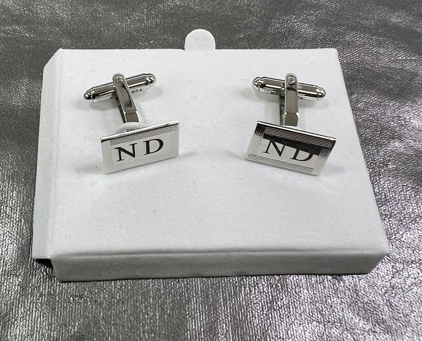 Silver cufflinks engraved with a two letter monogram on a white display