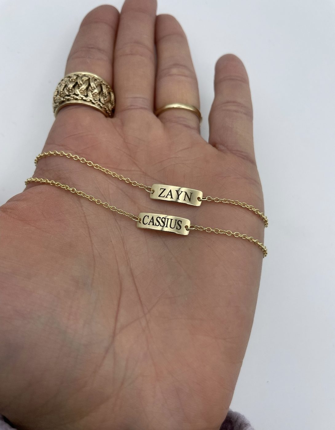 A hand wearing several thin gold rings engraved with names